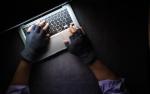 Przed laptopem siedzi haker w rękawiczkach.