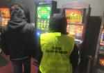 funkcjonariusz celno-skarbowy i osoba w kurtce stoją przy 3  maszynach do gier