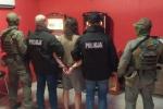 Funkcjonariusze KAS i Policji w trakcie kontroli salonu gier trzymają pod ręce mężczyznę skutego w kajdanki 