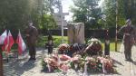 Przy pomniku stoi dwóch żołnierzy, a na ziemi leżą wiązanki kwiatów.