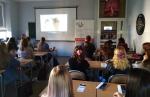 Uczniowie Pierwszego Liceum Ogólnokształcącego we Włoszczowie siedzą w ławkach i oglądają prezentację multimedialną 
